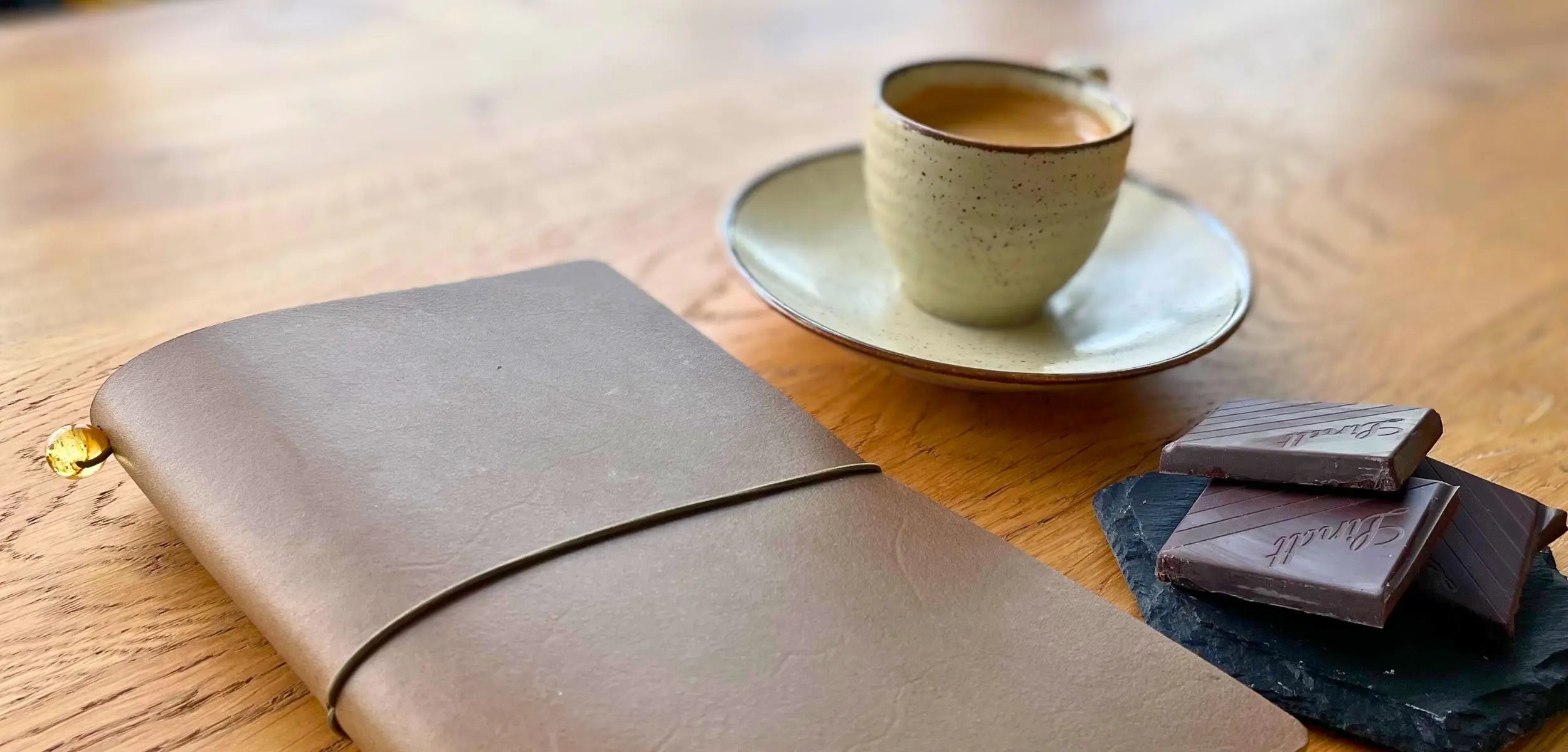 Handmade army green leather traveler’s journal resting on a wooden table beside coffee and chocolate, perfect for capturing your adventures.