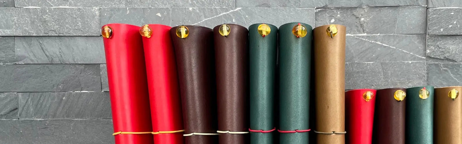 Handmade leather traveler’s journals by Bielinis displayed on grey brick background and wooden table—crafted for storytellers and explorers.