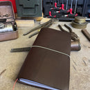 Dark brown handmade leather Atlas traveler’s journal in a rugged workshop setting, crafted for durability and style.