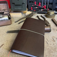 Dark brown handmade leather Atlas traveler’s journal in a rugged workshop setting, crafted for durability and style.