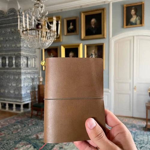 Handmade army green leather traveler's journal being held inside a historic museum room