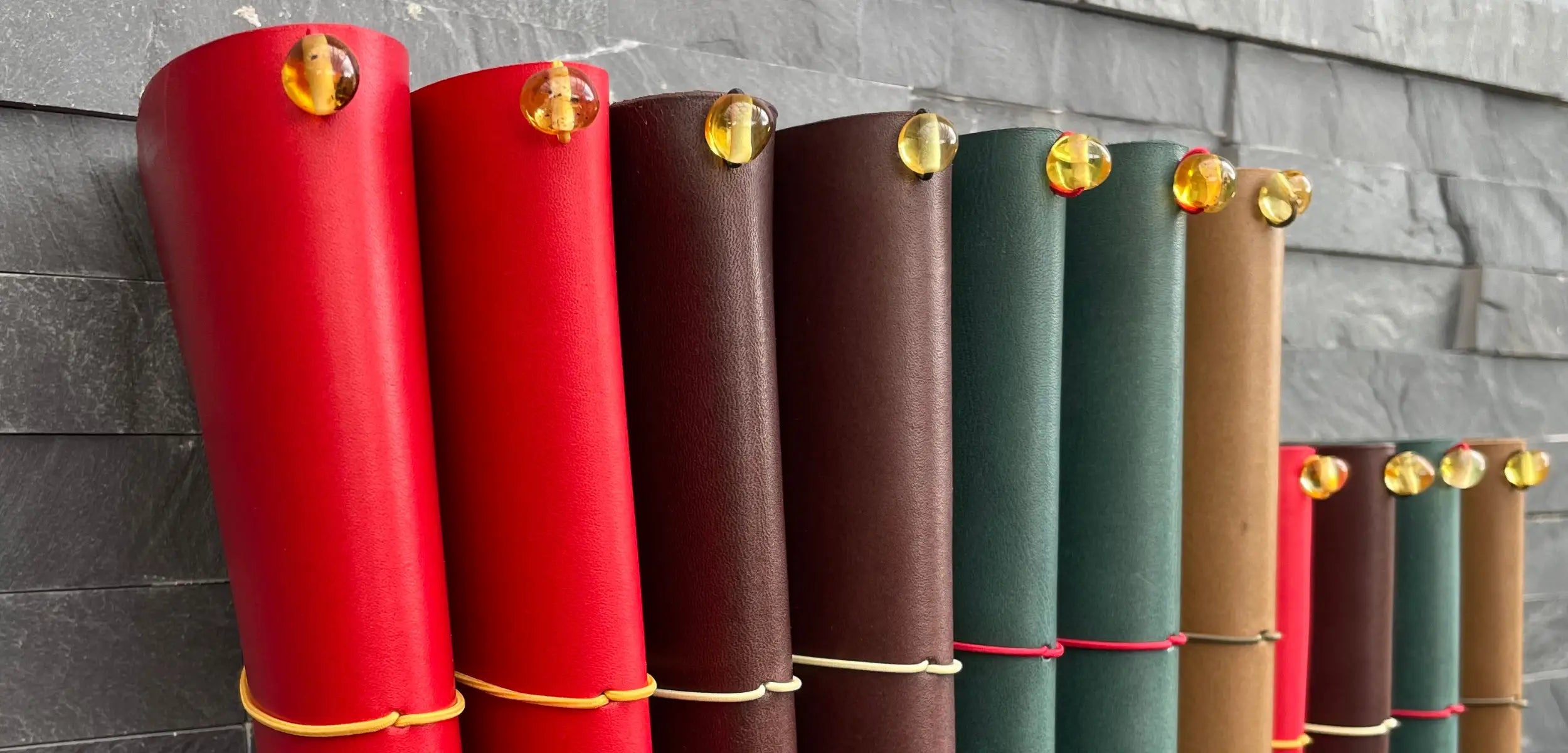 Close-up of handmade leather traveler’s journals with elastic cords and Baltic amber charms in various colors—crafted for durable, stylish storytelling.