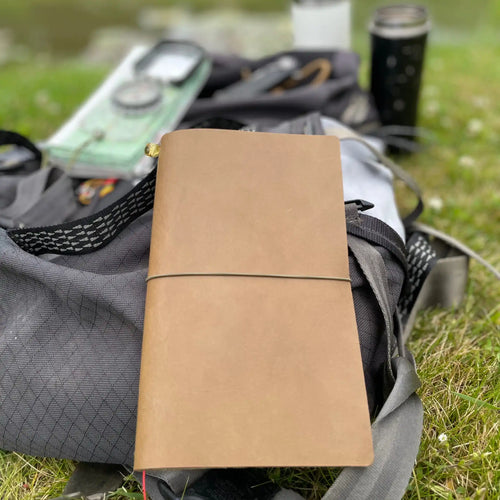 Handmade army green traveler’s journal from Bielinis, placed outdoors with backpack, map, and compass—perfect for explorers and adventurers.