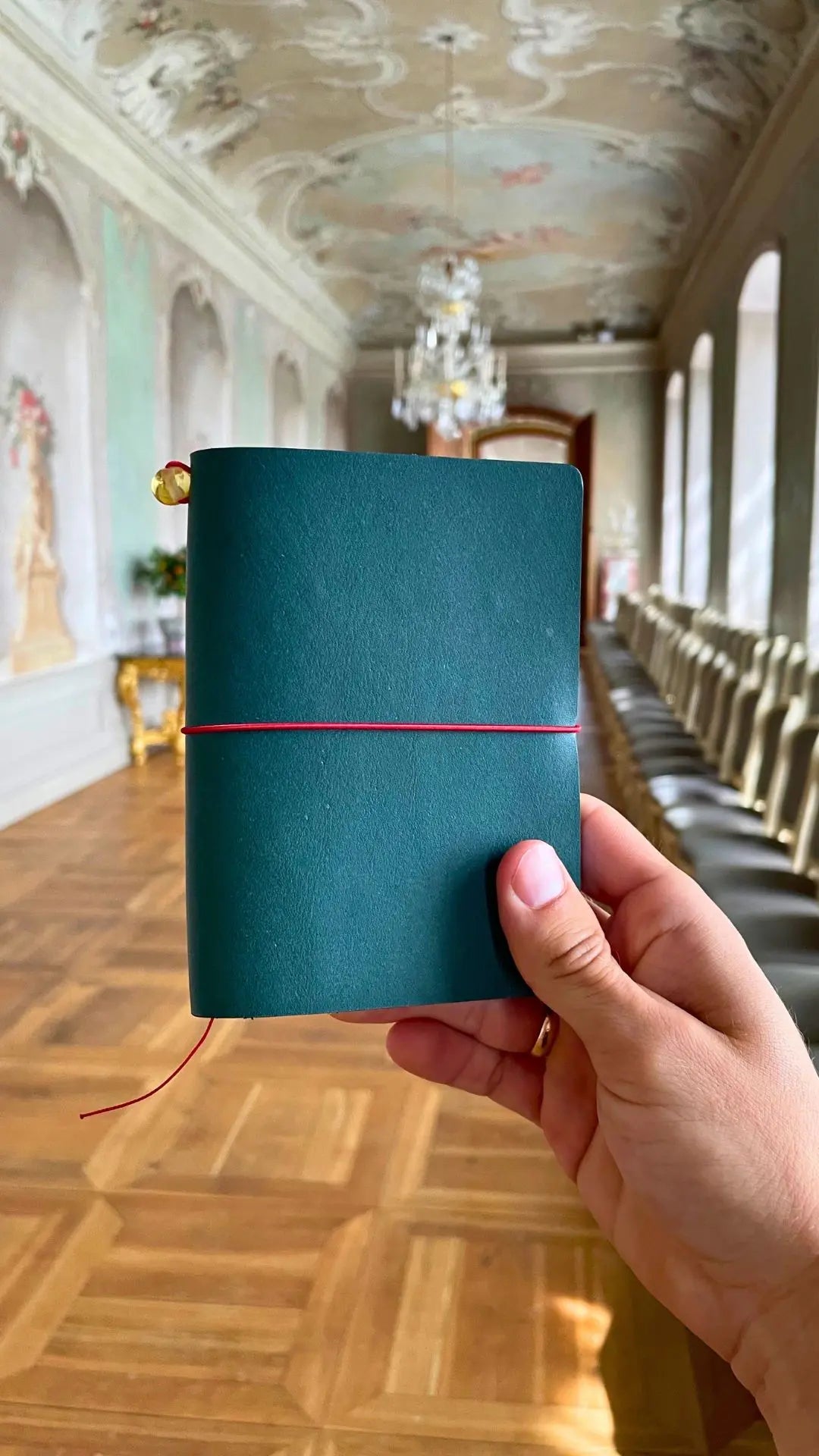 holding-handmade-Bielinis-travelers-journal-rundales-palace-petrol-blue-leather-vellum_jpg.webp