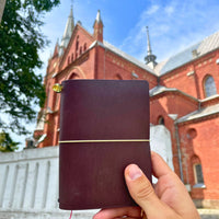 Hand holding a dark brown handmade leather traveler’s journal, Vellum size, crafted for durability and style.