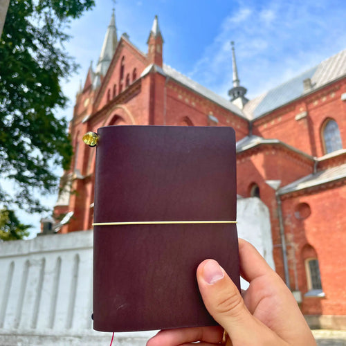 Hand holding a dark brown handmade leather traveler’s journal, Vellum size, crafted for durability and style.