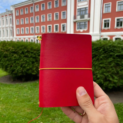 Hand holding a red handmade leather traveler’s journal, Vellum size, crafted for durability and style for each day use and every trip.