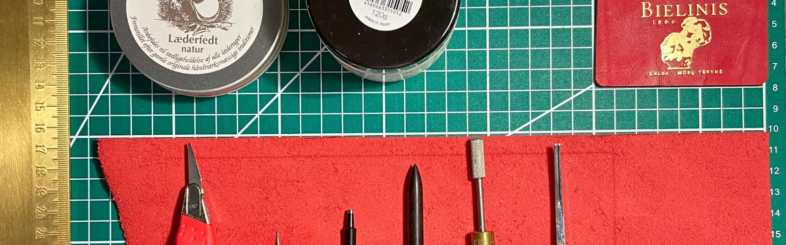 Leathercraft tools and care creams on cutting mat, essentials for maintaining handmade leather journals and accessories.