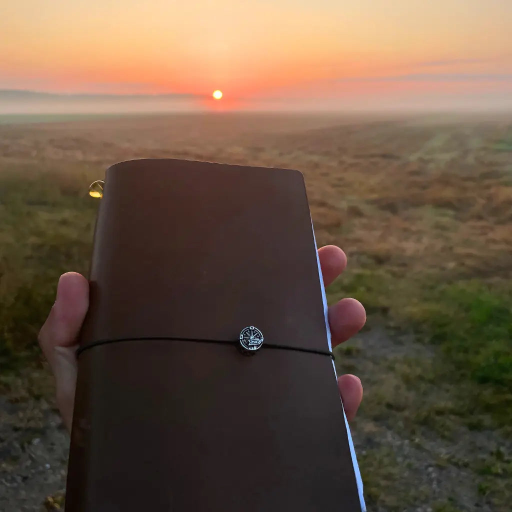 traveler-holding-bielinis-army-green-atlas-journal-at-sunrise.webp